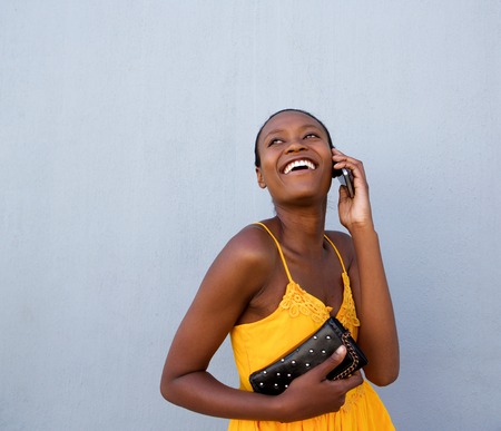 Portrait of young african lady talking on cellphone against gray wall