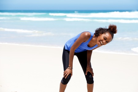 Portrait of healthy young african woman in sportswear standing on the beach and laughingの写真素材