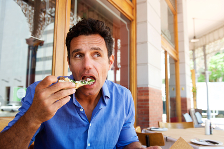 Portrait of an older handsome man eating pizza at outdoor restaurantの写真素材