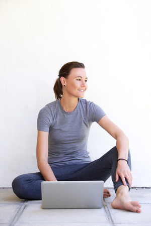 Portrait of happy young woman sitting on floor in patio with a laptopの写真素材