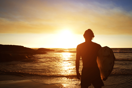 Silhouette of male surfer watching the sunset at the beachの写真素材