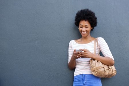 Portrait of smiling african woman with bag looking at mobile phone