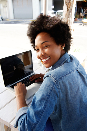 Portrait of a cool young african woman working on laptop at outdoor cafeの写真素材