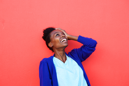 Portrait of young african female laughing with her hand on head against red backgroundの写真素材