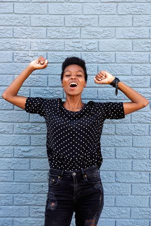 Portrait of excited african american woman celebrating against gray wallの写真素材