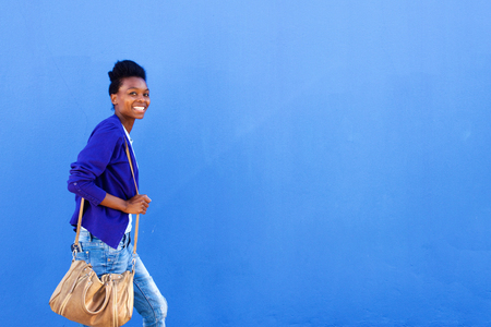 Portrait of smiling young african woman walking against blue wallの写真素材