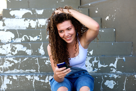 Portrait of smiling teen with hand in hair sitting with cellphoneの写真素材