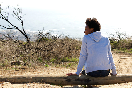 Rear view portrait of young woman sitting outdoors on a log and looking awayの写真素材
