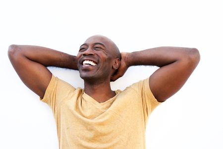 Portrait of relaxed young black man standing with his hands behind head against white wallの写真素材