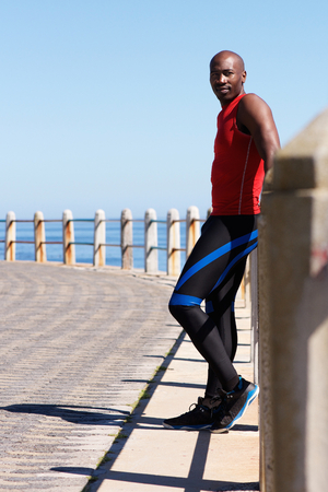 Full length portrait of fit young african man standing at seaside promenadeの写真素材