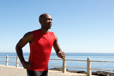 Portrait of fit young african sportsman jogging outdoors on the promenade by the seaの写真素材