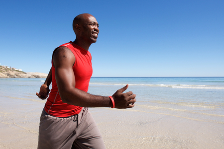 Side portrait of fit and happy young black man walking along the seashoreの写真素材