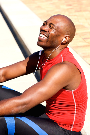 Portrait of happy young sports man relaxing outdoors and listening to music on headphones