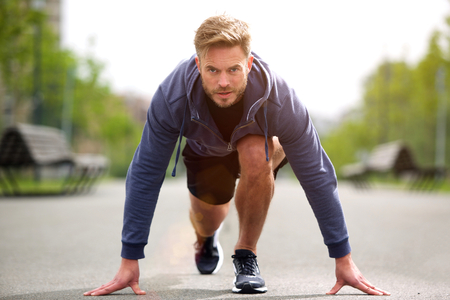 Portrait of healthy runner in starting position outside