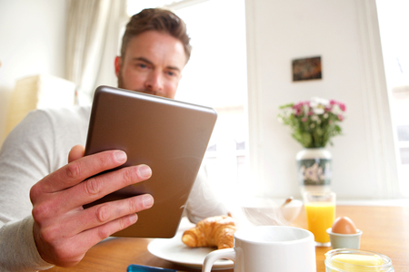 Portrait of older man holding tablet over breakfastの写真素材
