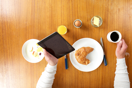 Portrait of hands holding tablet and coffee at breakfast tableの写真素材
