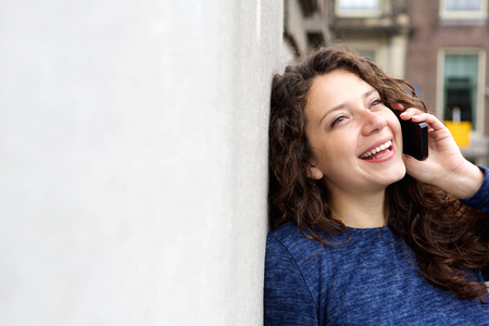 Close up portrait of smiling young woman leaning to a wall outdoors and talking on cell phoneの写真素材
