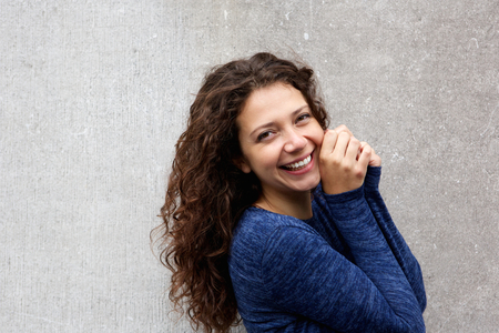 Close up portrait of cute young female model smiling at camera against gray wallの写真素材