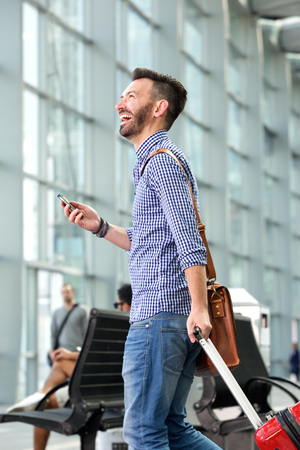 Side portrait of cheerful mature man walking with bag and mobile phoneの写真素材