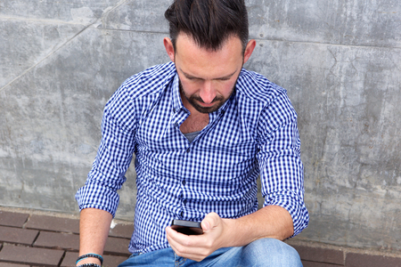 Close up portrait of middle aged man sitting outside and using mobile phoneの写真素材