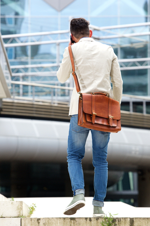 Rear portrait of man walking outdoors and talking on cell phoneの写真素材
