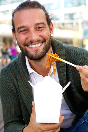 Portrait of smiling man eating take out food with chopsticksの写真素材