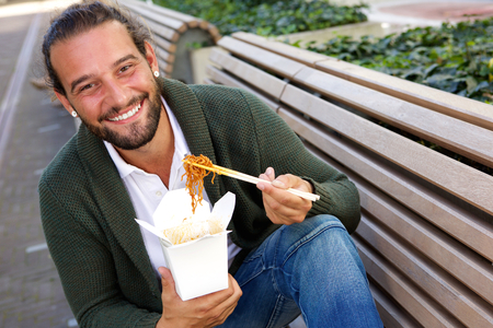 Portrait of smiling man eating fast food noodles with chopsticksの写真素材