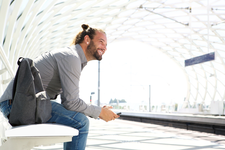 Portrait of smiling man with cell phone waiting at train platformの写真素材