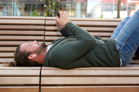 Portrait of man lying down on bench with earphonesの写真素材