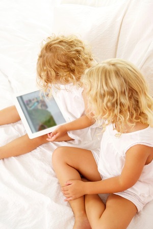 Top view portrait of two little girls using digital tablet on bedの写真素材