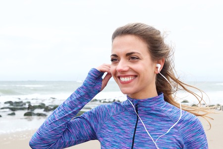 Close up portrait of smiling sporty woman smiling on beach with headphonesの写真素材