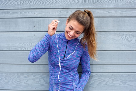 Portrait of happy woman putting on headphones by wallの写真素材