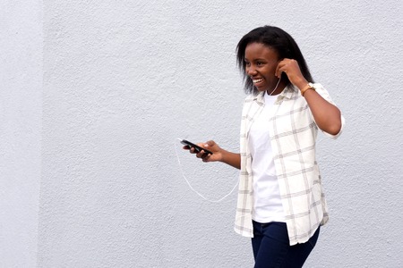Happy young african woman walking and listening music on mobile.の写真素材