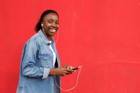 Portrait of happy african woman listening music against red background.の写真素材