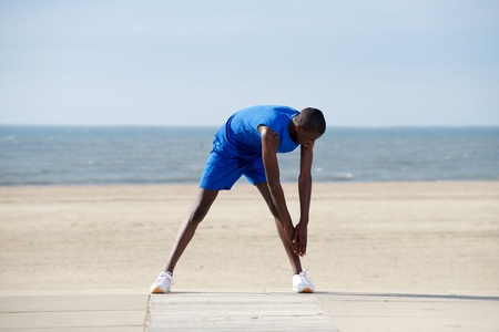 Full body portrait of young african american man stretching on the beach