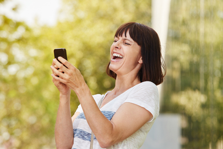 Close up portrait of older woman laughing looking at smart phoneの写真素材