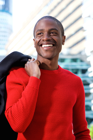Close up portrait of smiling african man holding coat over shoulder in the cityの写真素材