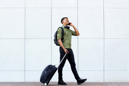 Full length portrait of smiling young man walking with luggage and mobile phoneの写真素材