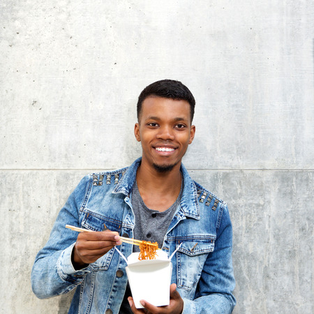Portrait of smiling african american man with noodles in fast food boxの写真素材