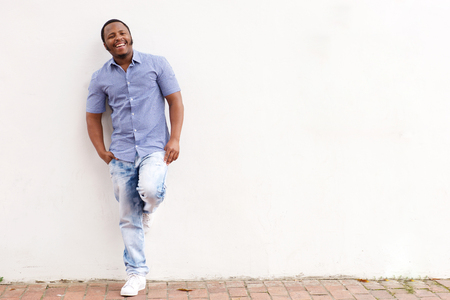 Full length portrait of smiling young african american man leaning against white wallの写真素材
