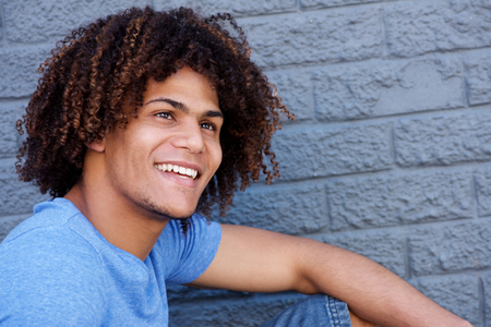 Close up side portrait of cool man with curly hair smiling against gray wallの写真素材
