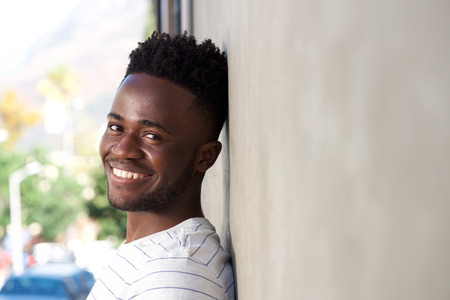Close up side portrait of smiling handsome man leaning on wall outsideの写真素材