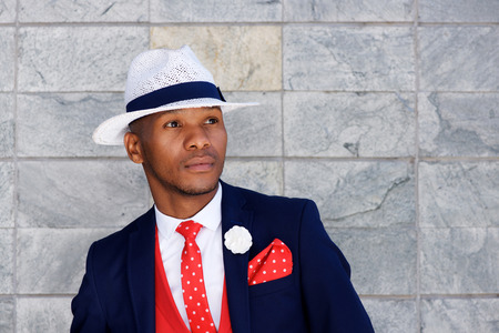 Close up portrait of handsome young african man in suit and hat looking away and thinking