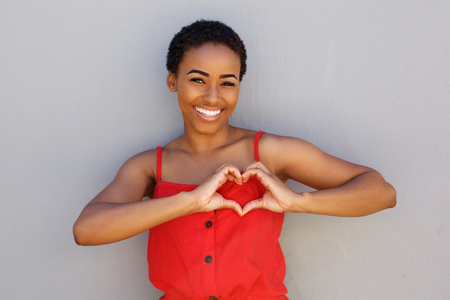 Portrait of smiling young african american woman with heart shape hand signの写真素材