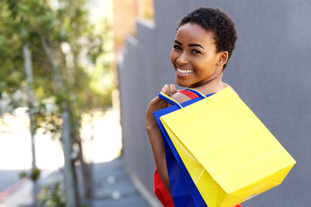 Portrait of beautiful young black woman smiling with shopping bags outsideの写真素材