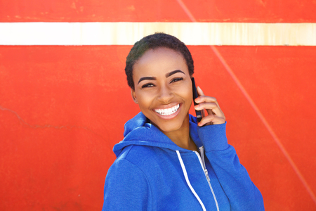 Portrait of cool young woman talking with cellphone against red wall