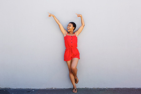 Full body portrait of cheerful young woman pointing with arms raisedの写真素材