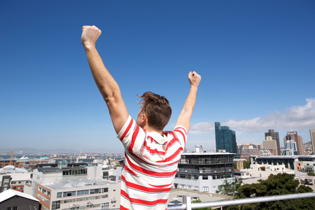 Portrait from behind of young man with arms raised outsiceの写真素材