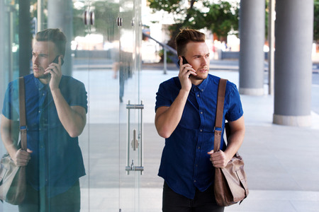 Portrait of cool fashion guy walking with cellphone and bagの写真素材