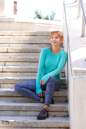 Full body portrait of smiling female athlete resting on steps outsideの写真素材